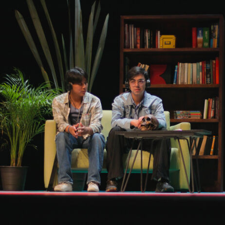 Photo extraite de la Conférence des absents : deux personnes sont sur scènes avec un casque sur les oreilles, assis sur un canapé et devant une table.