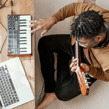 Un homme joue de la guitare, avec un petit clavier de panneau et un ordinateur branché (mao, musique assistée par ordinateur)